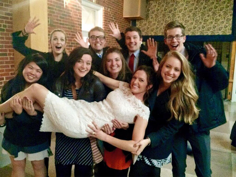 A group of people at a wedding hold up the bride in a vertical postion for a photo.