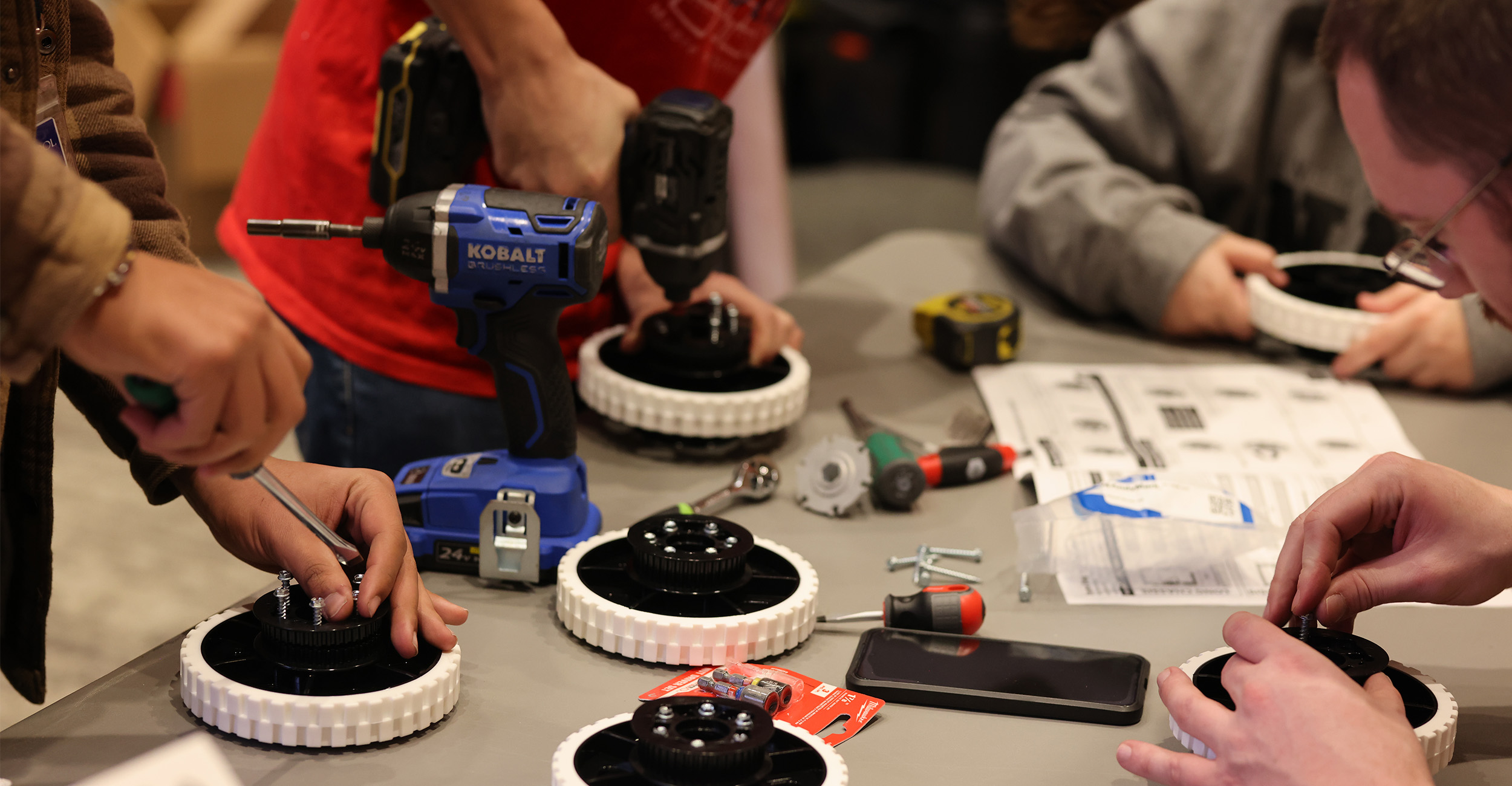 An up-close image of people working on wheels with screwdrivers and drills while looking over instructional manuals.