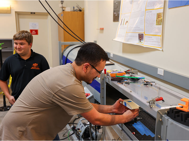 Two students working in a lab on a wind tunnel.