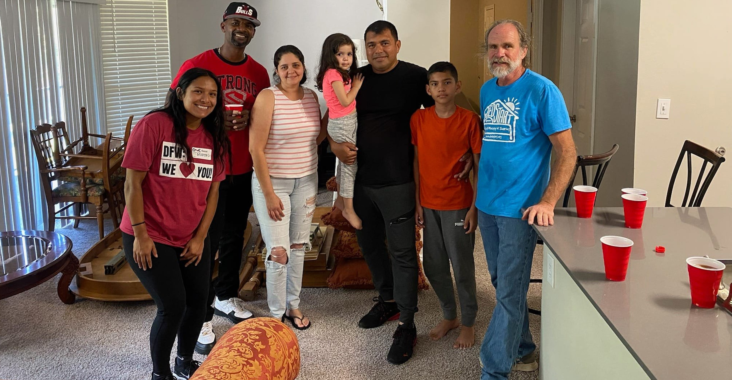 A group of people stand in a living room for a posed photo together.