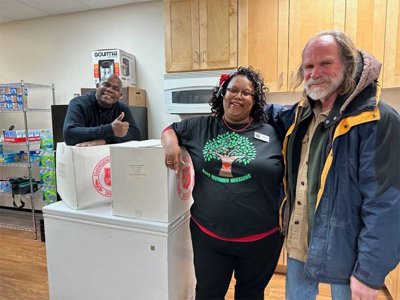 Three people stand smilling in a kitchen for a posed photo.