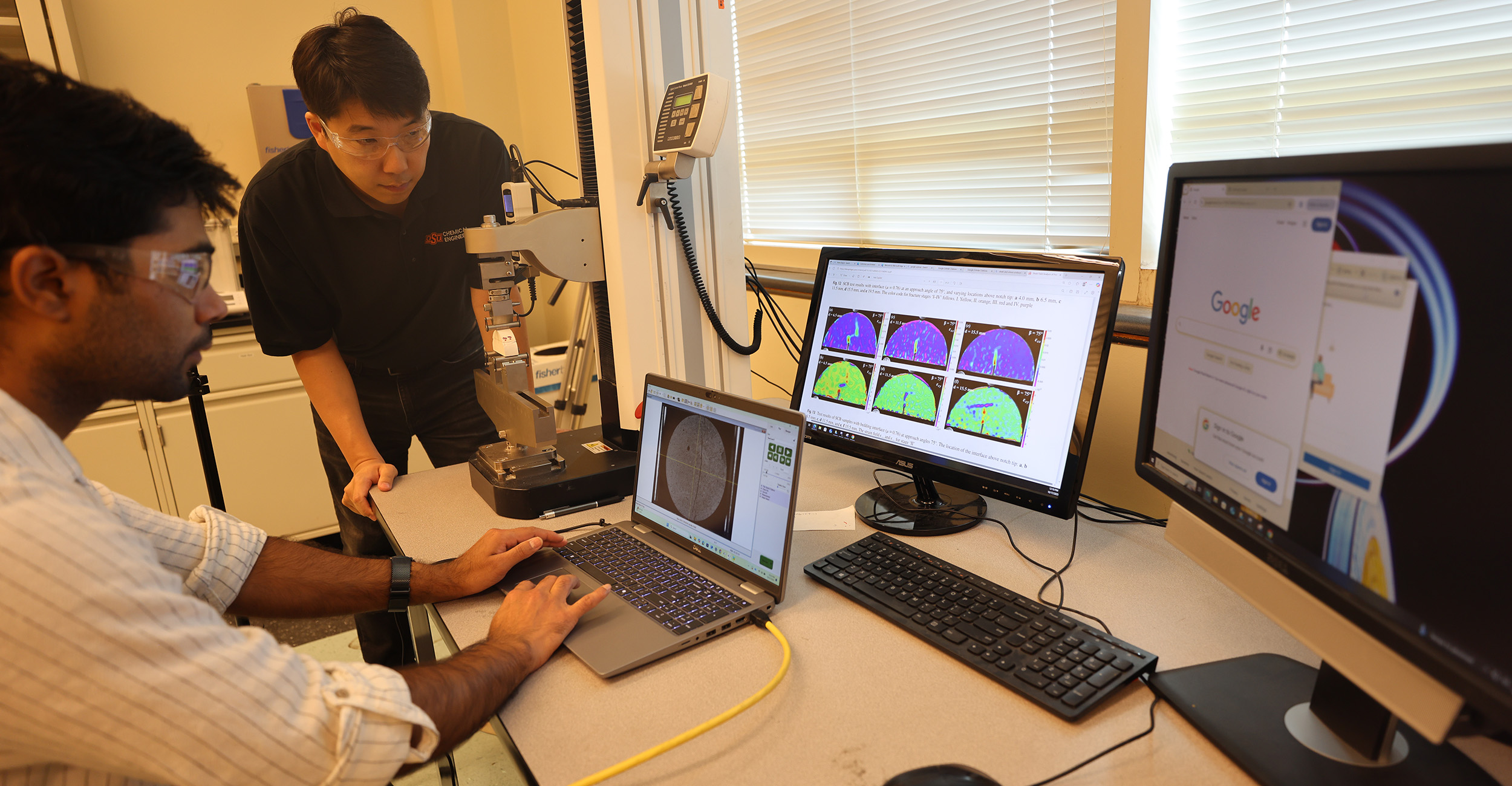 Dr. Hunjoo Lee, a professor in the Oklahoma State University School of Chemical Engineering, observes student Vishesh Bhadariya operating research equipment in Lee’s lab. The two are analyzing data and images displayed on computer monitors connected to testing machinery.