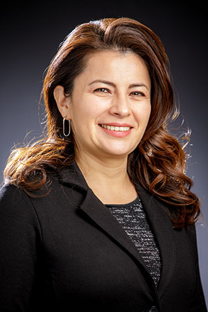 A woman wearing a black blazer over a black shirt, standing confidently with a neutral expression.