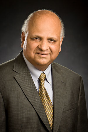 A man wearing a formal suit and tie, standing confidently with a neutral expression.