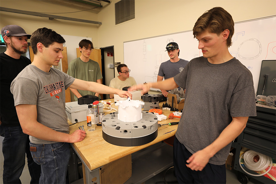 A group of students discuss an engine in a lab setting.