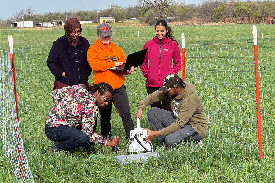 A group of five individuals gather around a machine for testing agriculture while standing in a field.