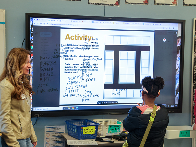 A female college students leads a young k12 female student through an architecture activity. 