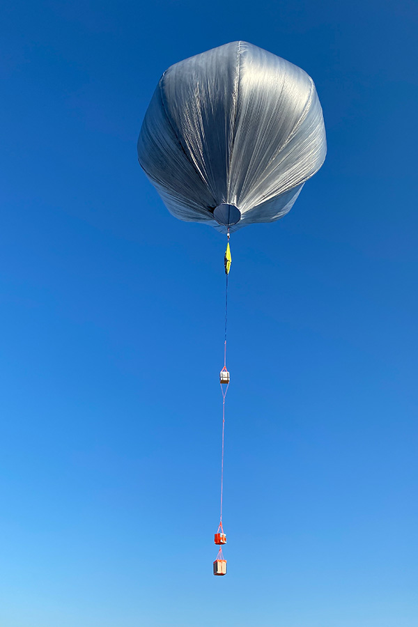 A balloon fitted with scientific monitoring equipment lifts off the ground.