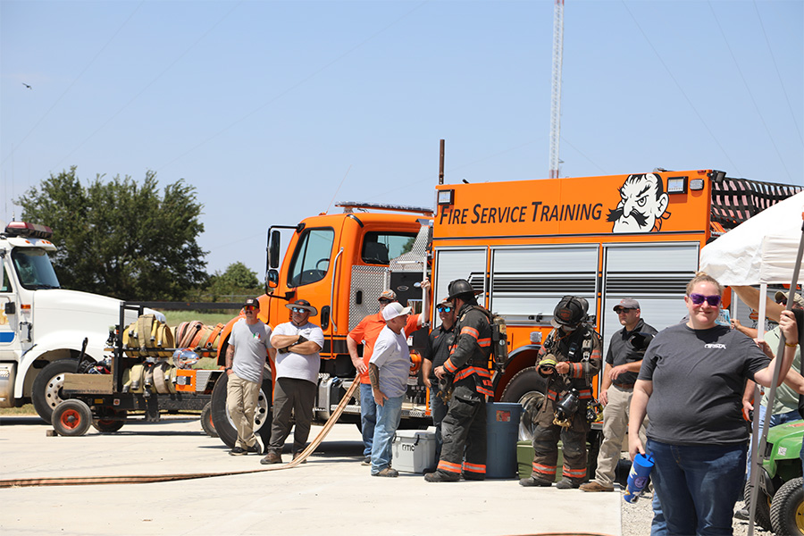 A group is gathered around an orange fire truck with OSU Fire Service Training's program logo.