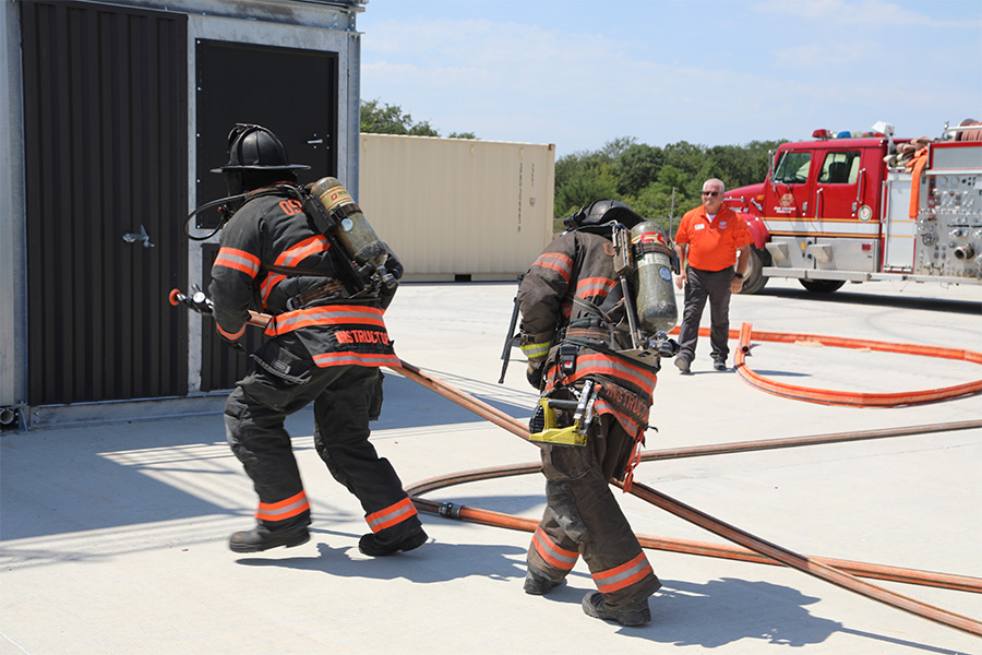 Two firefighters prepare a demonstration of suppressing a fire.