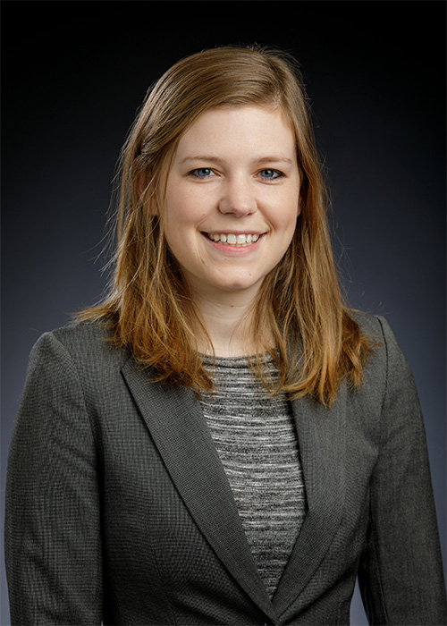 A headshot of a women in a dark grey blazer.