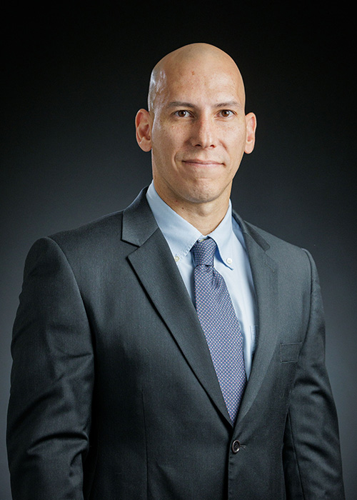 A headshot of a man in a dark grey suit.