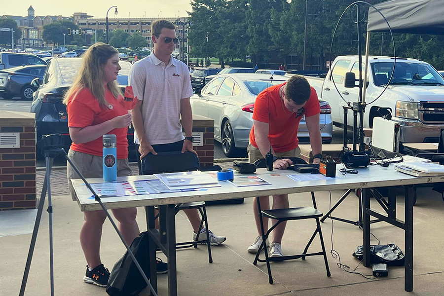 Three people stand near a table and collaborate while using radio equipment. 