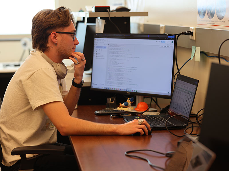 A student in a white shirt working on a computer program in a laboratory.