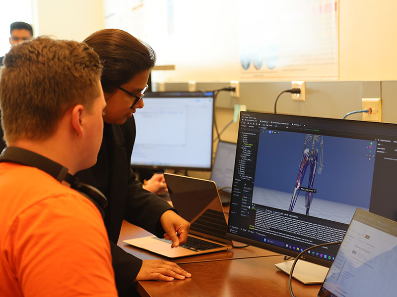 A professor looks at a student's computer screen as they discuss ways to improve the human body simulation.