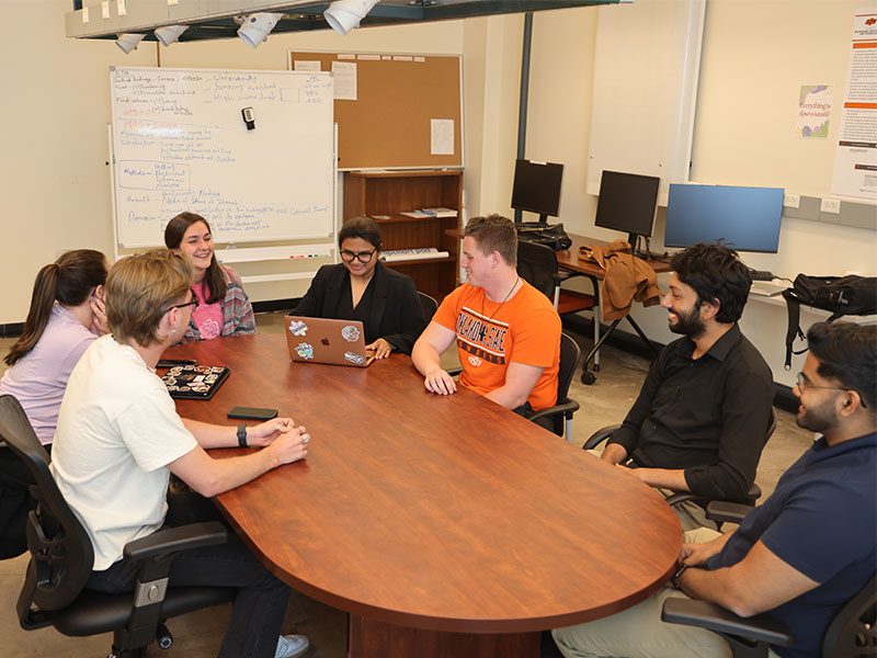 The CoPE lab members sit around a large oval shaped table, smiling.