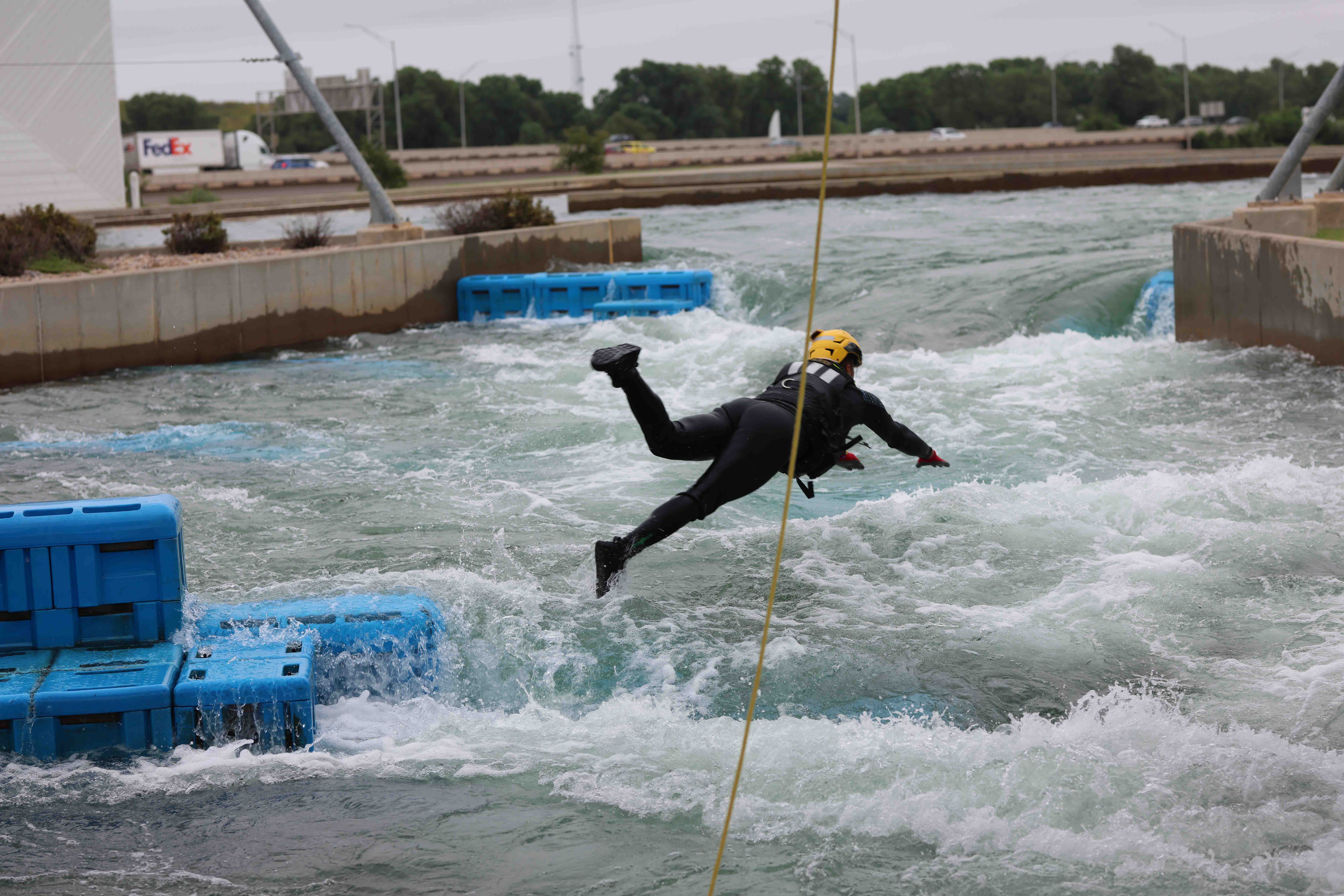 A person in a black wetsuit and helmet dives into rapids.
