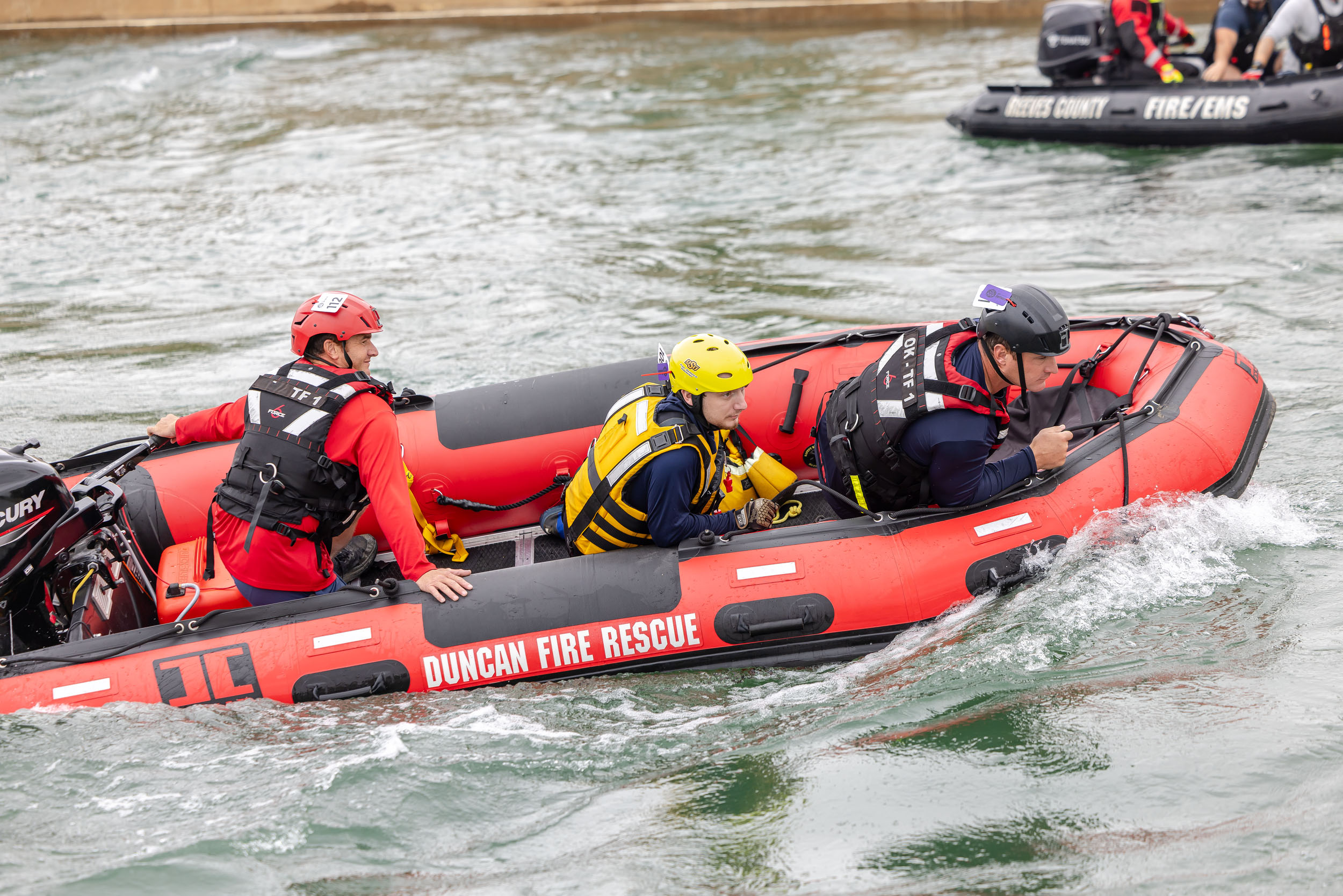 Several first responders sit in a red raft in a river. They are all dressed in helmets and life vests.