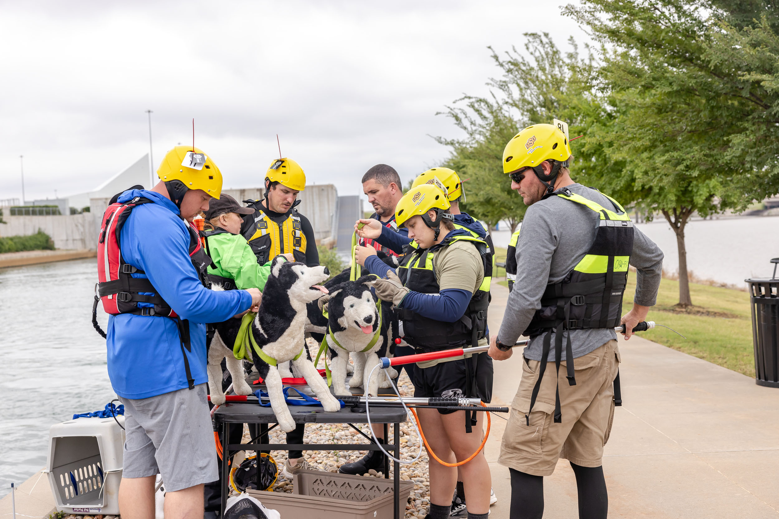 A group of people in helmets and life vests surround a table with rescue animal dummies.