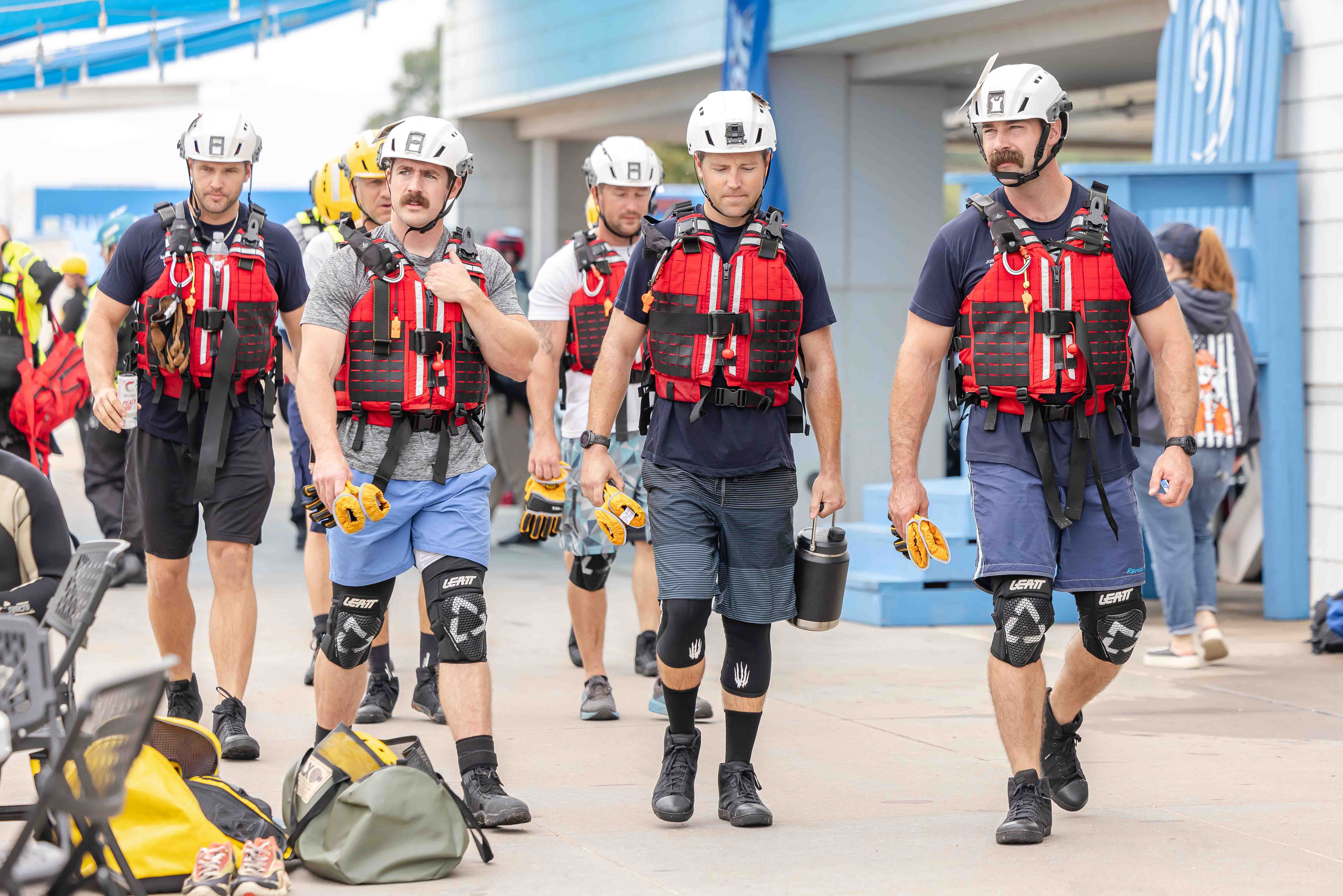 A group of men walk towards the camera dressed in red life vests, protective gear, and helmets.