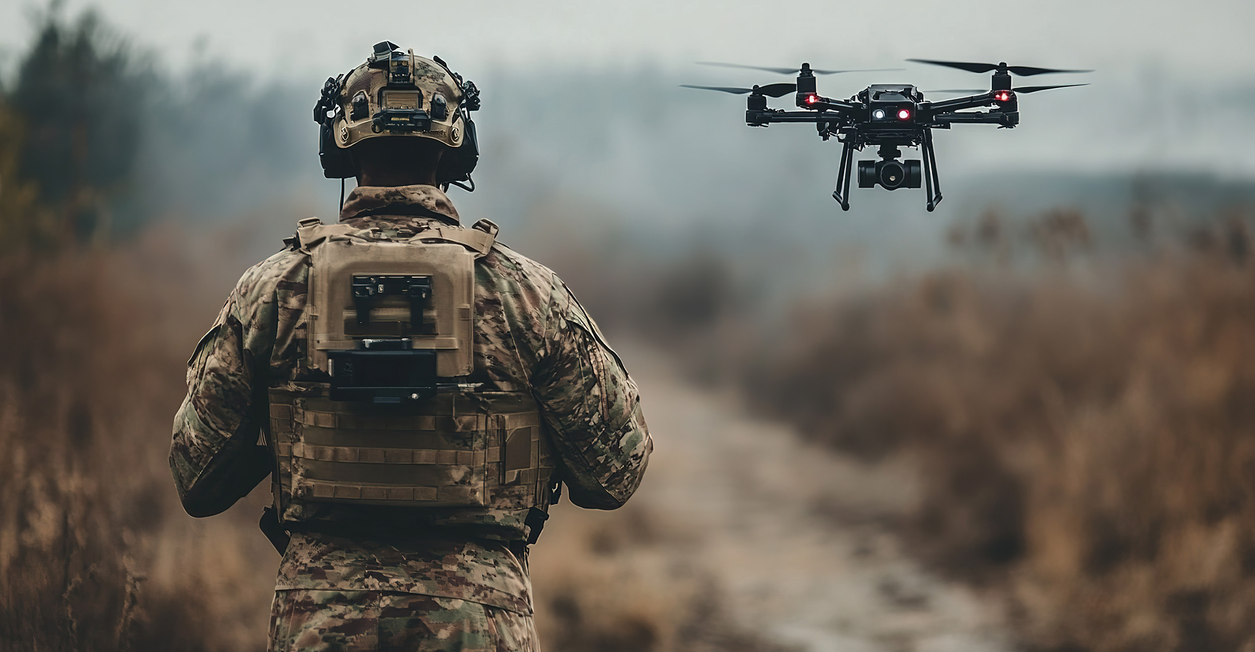 An individual dressed in a military combat uniform controls a drone while in a desert location.