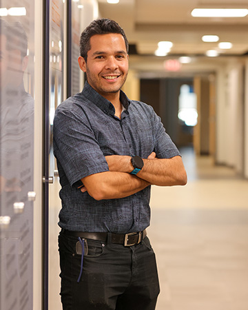A man dressed professionally poses in a long hallway for a headshot.