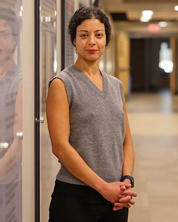 A professionally dressed woman poses in a long hallway for a headshot.