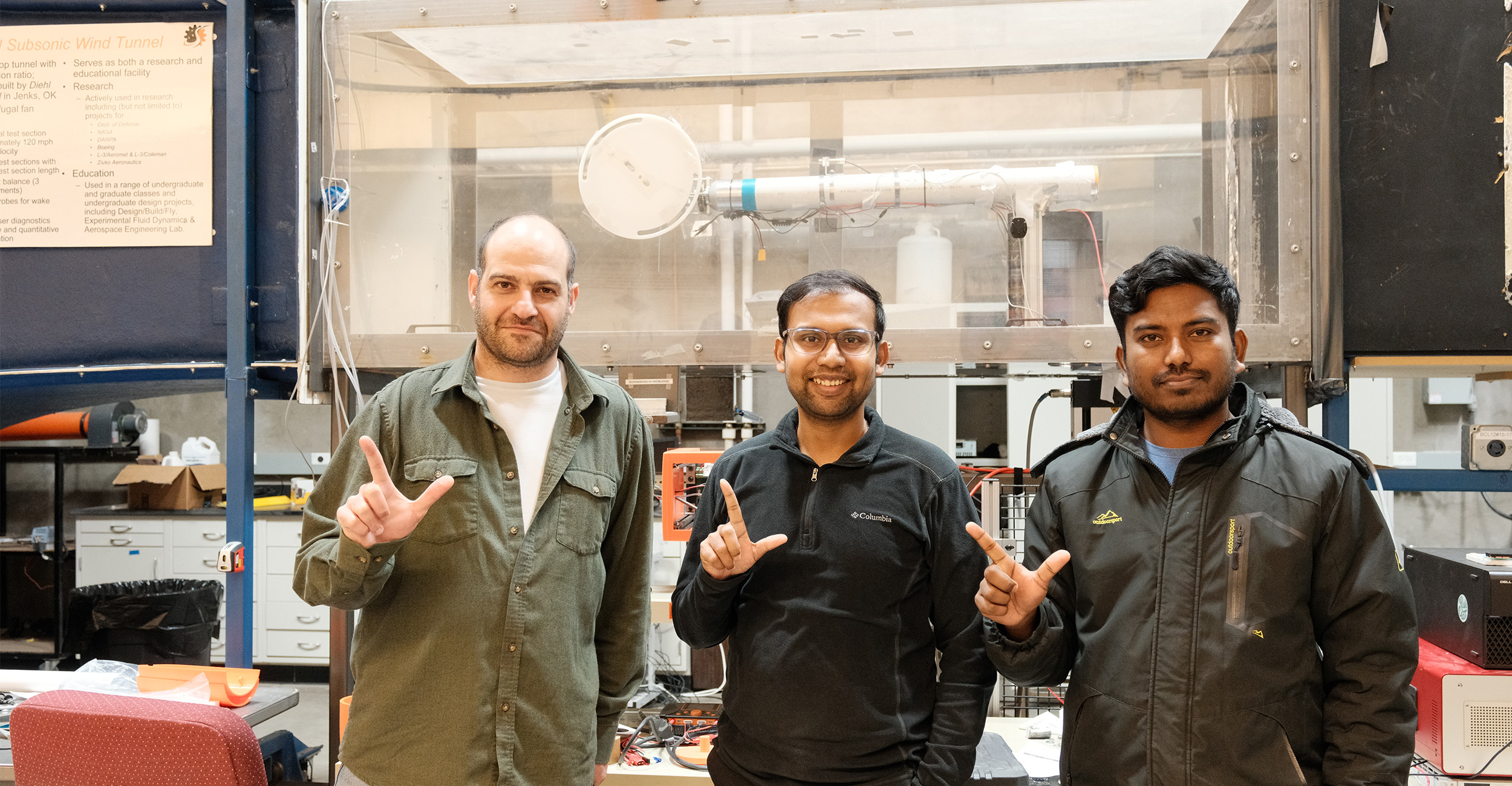 From left to right: Pedram Dabaghian, Dr. Halder and Ripon Sarker stand in front of a subsonic wind tunnel.