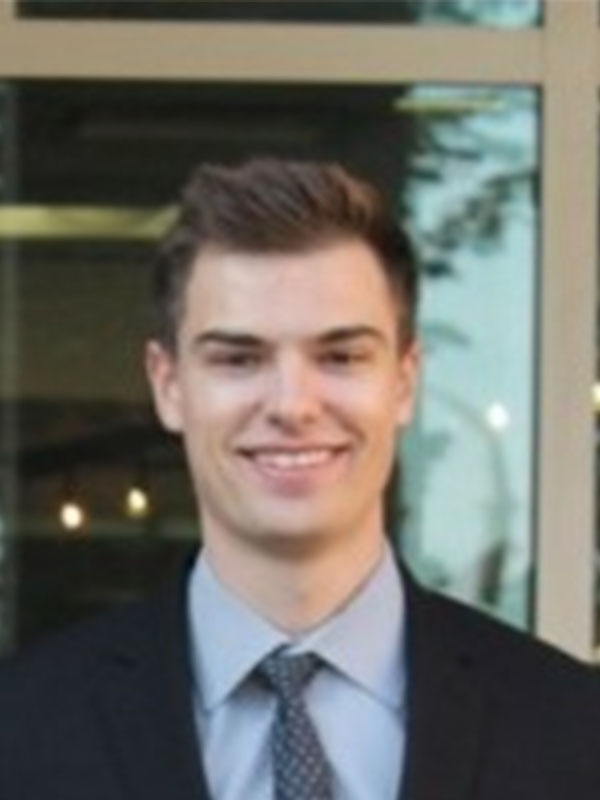A headshot of a young professional in a black suit.