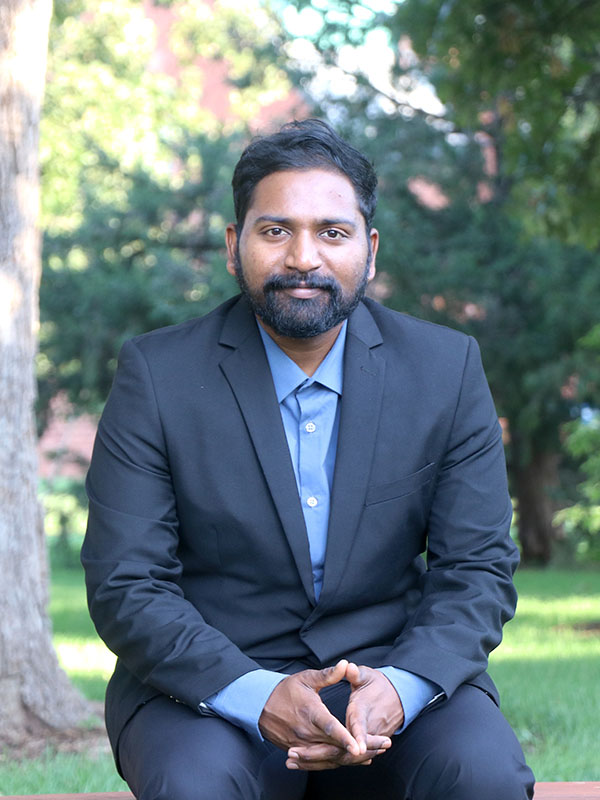 A young professional dressed in a navy blue suit poses in nature.