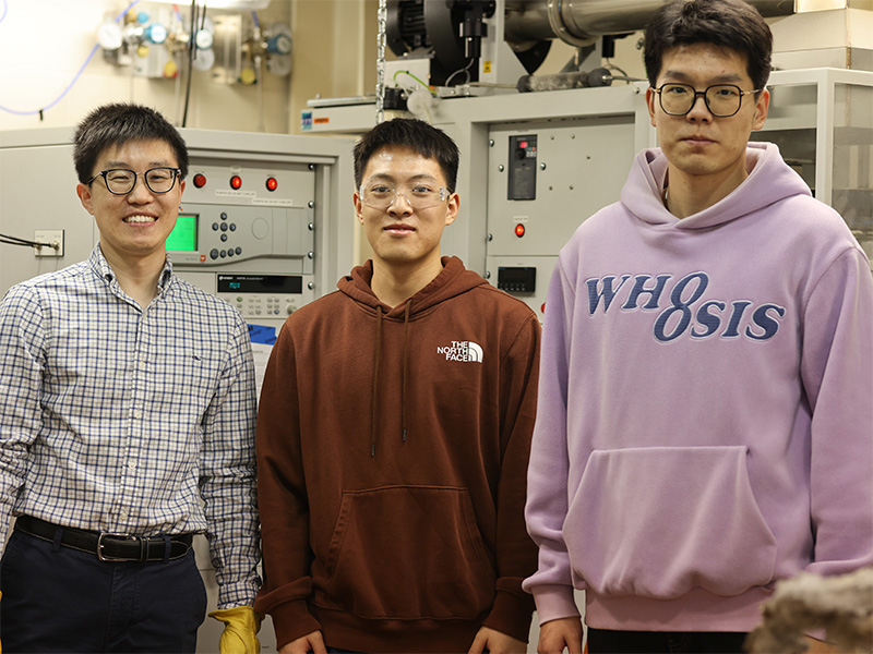 Trojica muškaraca stoje ispred istraživačke opreme u laboratoriju.