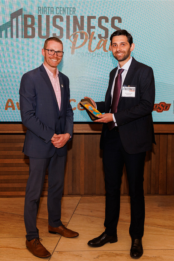 Two men in suits stand smiling after the man on the left had presented the man on the right an award.