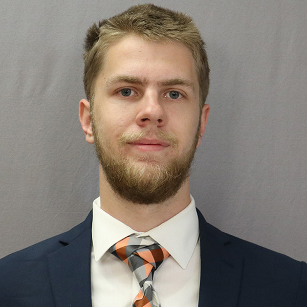 Trey Van Velsor is shown in his employee portrait from his job at Tinker Air Force Base. He is wearing a suit and tie, conveying a sense of professionalism.