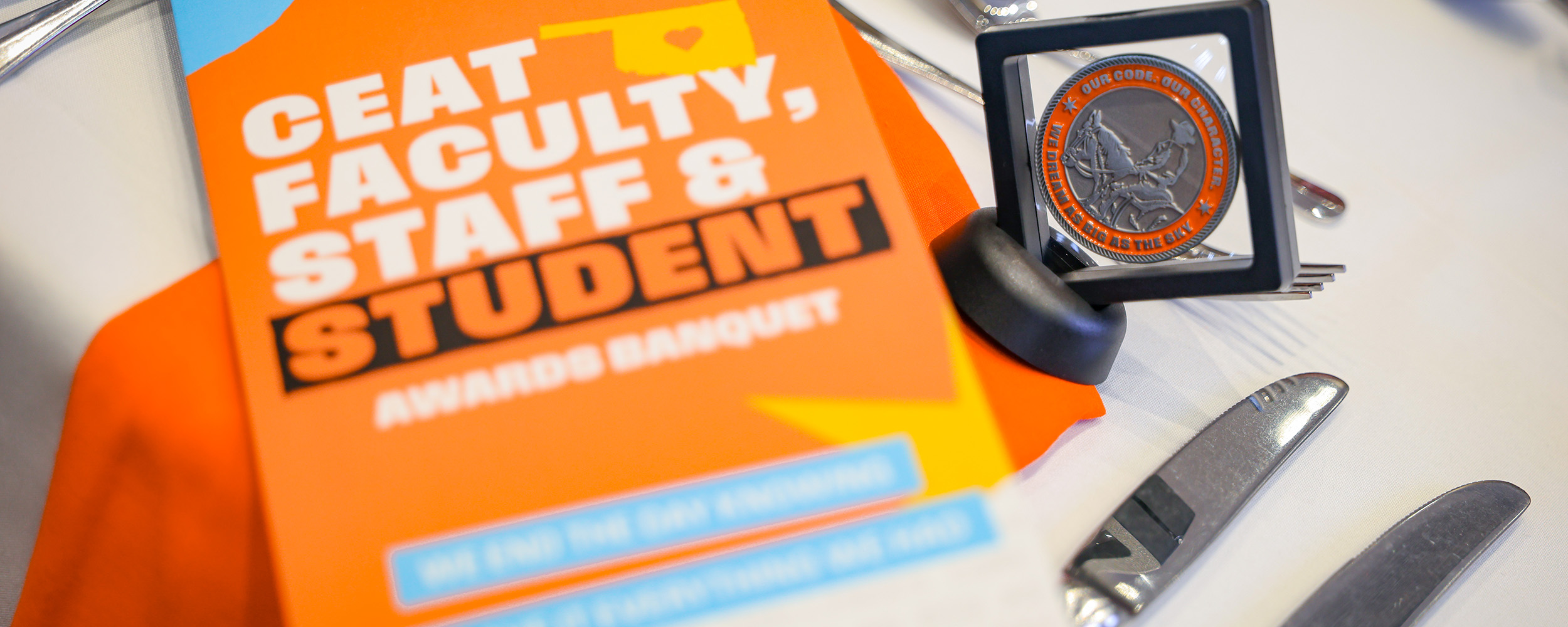 A close-up tabletop display shows a CEAT Faculty, Staff, and Student Awards Banquet program alongside a commemorative medallion, highlighting the event’s focus on recognition and honors.