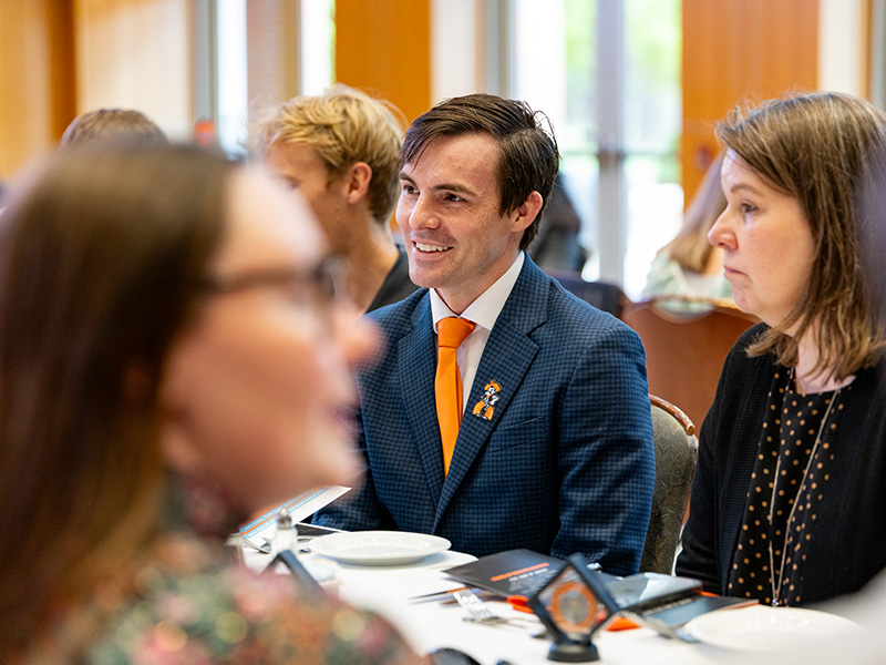 Attendees sit at a round table during a CEAT Faculty, Staff, and Student Awards Banquet, with place settings, printed programs, and a visible event medallion in an indoor dining space.