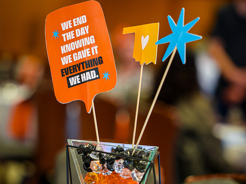 A tabletop centerpiece displays orange and blue decorative signs on sticks, including a message reading “We end the day knowing we gave everything we had,” emphasizing the celebratory theme of a CEAT Faculty, Staff, and Student Awards event.