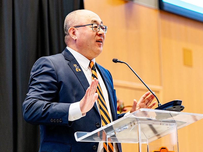 A speaker stands at a clear podium addressing an audience during a CEAT Faculty, Staff, and Student Awards Banquet, emphasizing the formal program and leadership remarks portion of the event.
