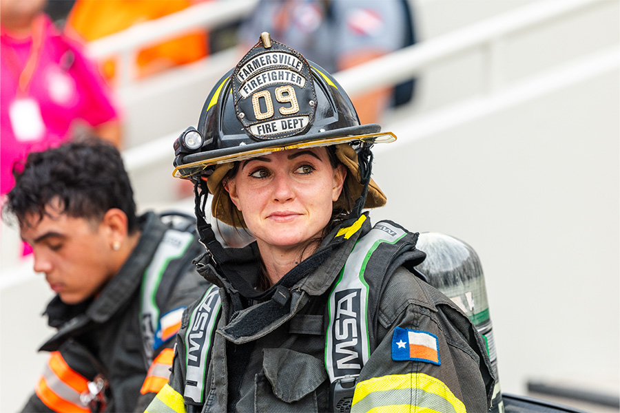 A close-up photograph shows a female firefighter wearing dark protective gear and a black helmet.