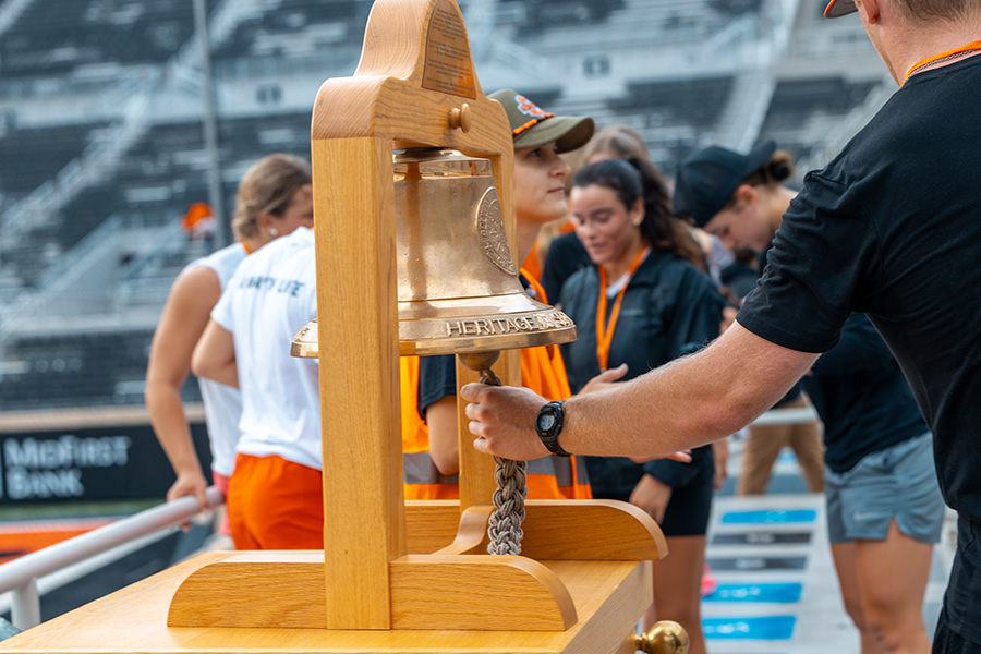 A close-up photograph shows a large wooden bell structure at an outdoor event