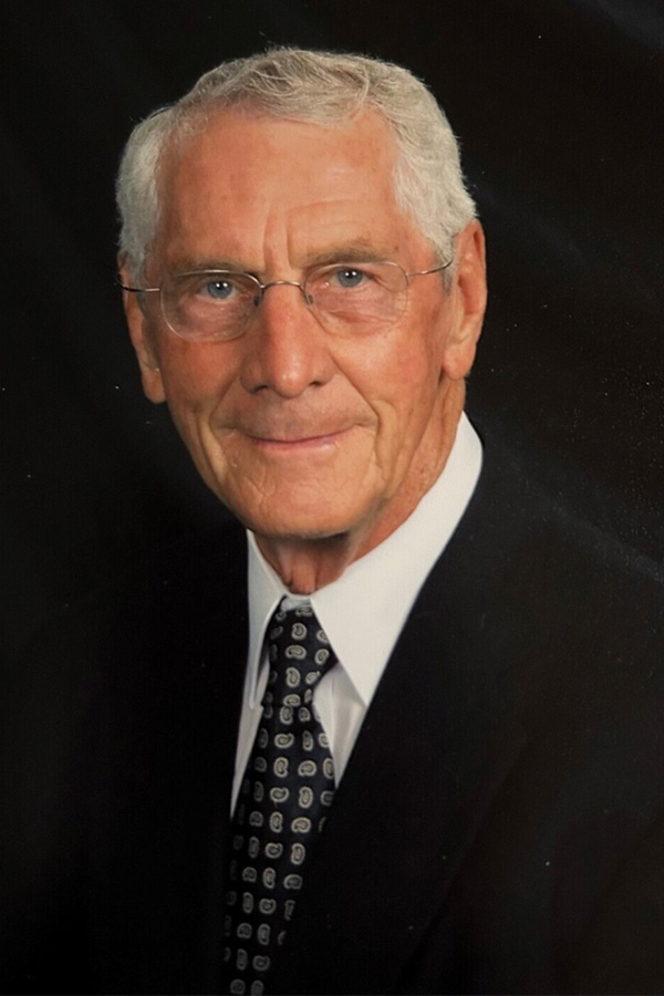 A head-and-shoulders portrait of an older man against a solid black background.