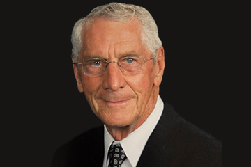 A head-and-shoulders portrait of an older man against a solid black background.