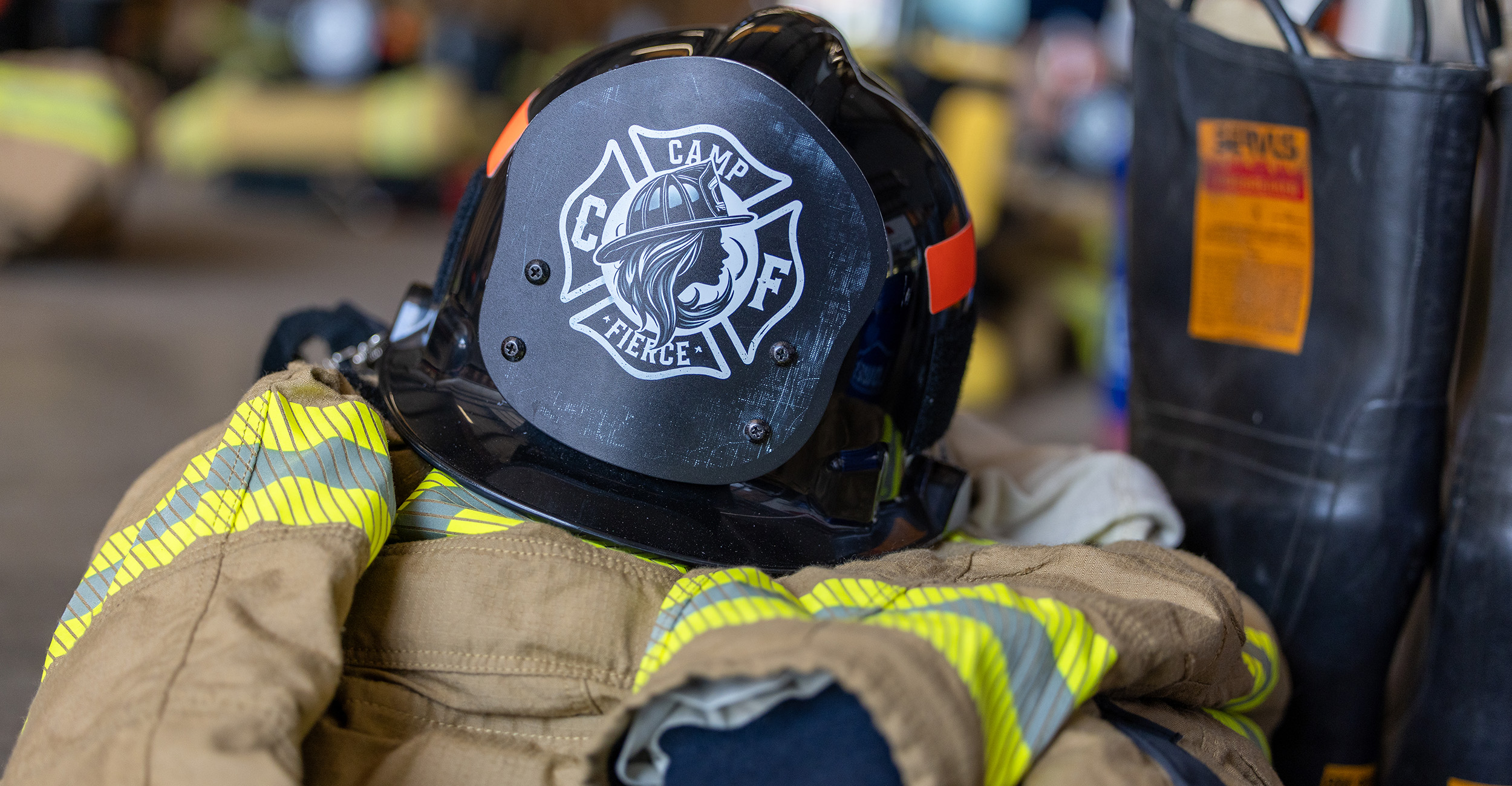 Close-up of a firefighter helmet labeled “Camp Fierce” resting on turnout gear and equipment.