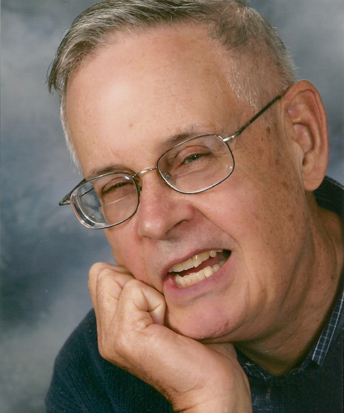 Portrait of a person wearing glasses resting their chin on their hand against a neutral backdrop, highlighting a close-up headshot.
