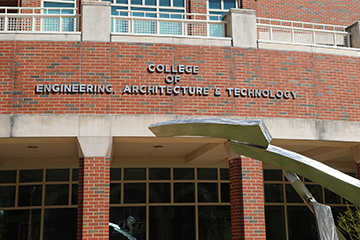 Exterior view of Oklahoma State University’s College of Engineering, Architecture and Technology building with its name displayed on the brick facade and a metal sculpture in the foreground, highlighting the campus academic facility.