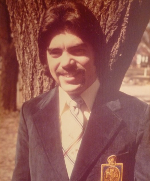 A vintage-style outdoor portrait shows a person in a suit and tie standing in front of a tree.