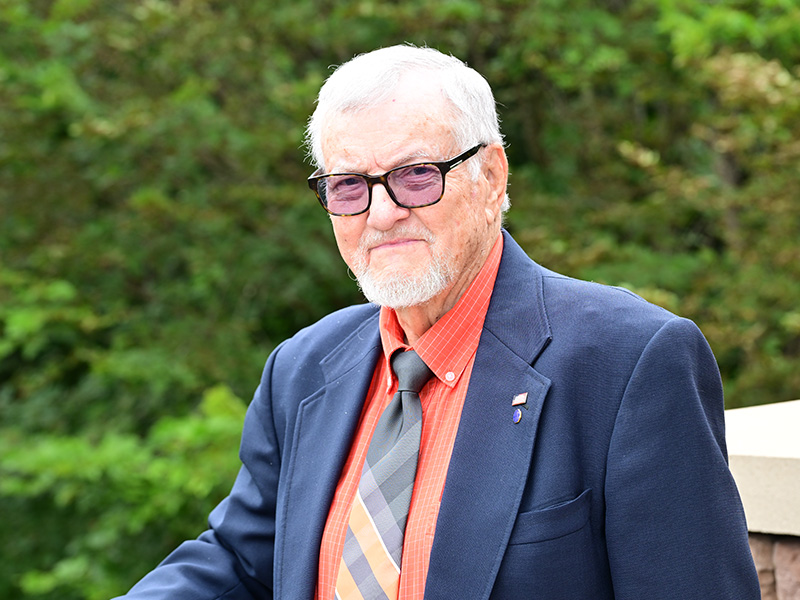 Man wearing glasses wearing a black blazer, orange shirt and a tie