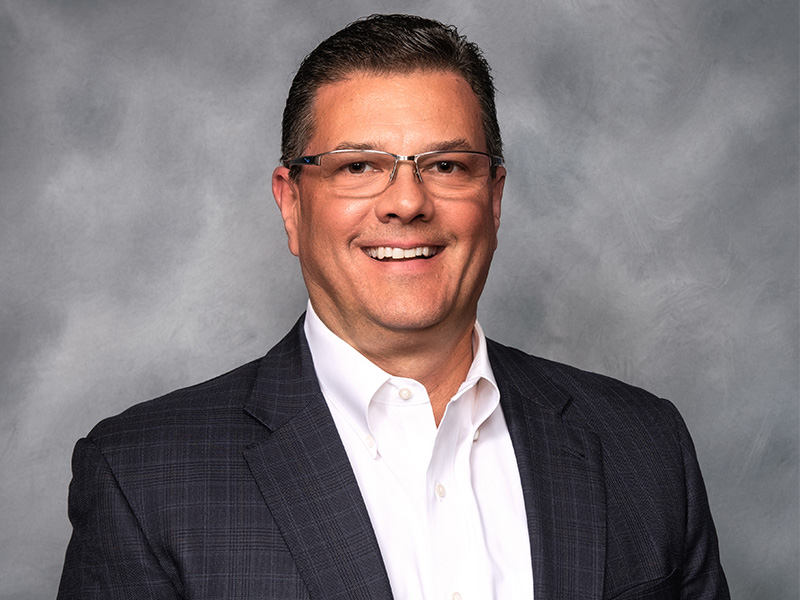 Man with glasses wearing a black blazer and white dress shirt smiling for a portrait