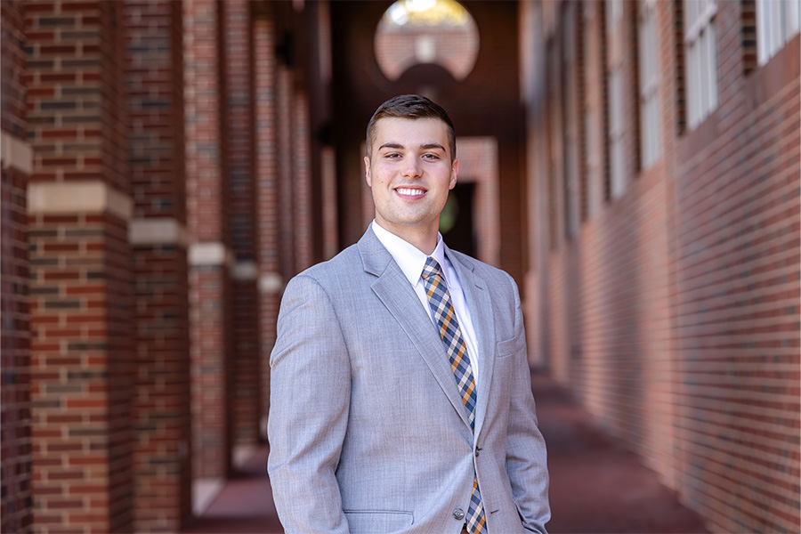 Man stands in front of a brick building with a light gray suit and tie