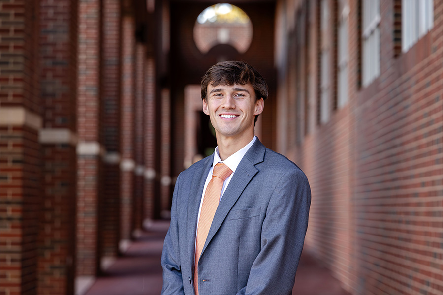 Man stands in front of a brick building with a dark gray suit and tie