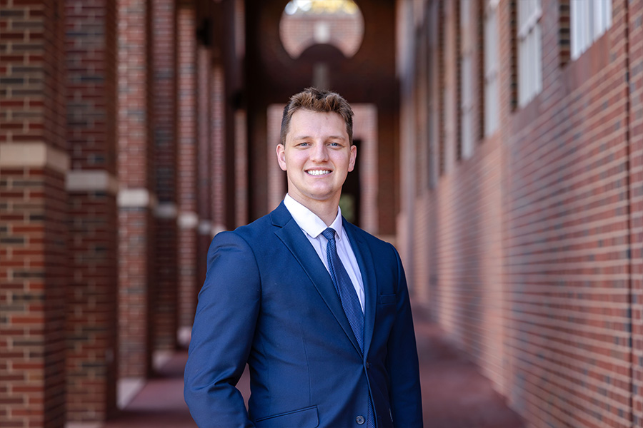 Man stands in front of a brick building with a blue suit and tie